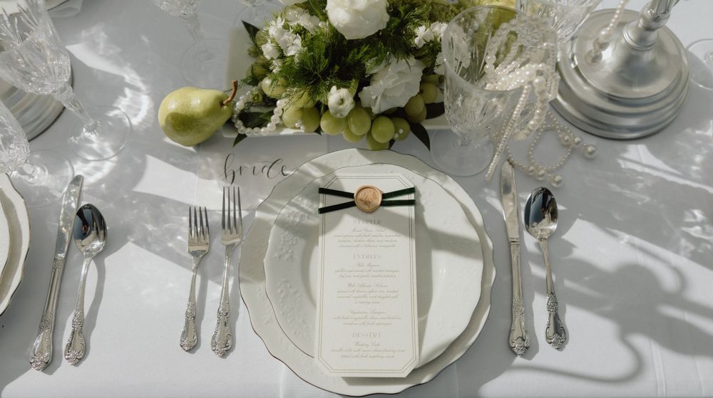 Elegant white and silver wedding place setting with floral centerpiece and menu card on crisp linen tablecloth.