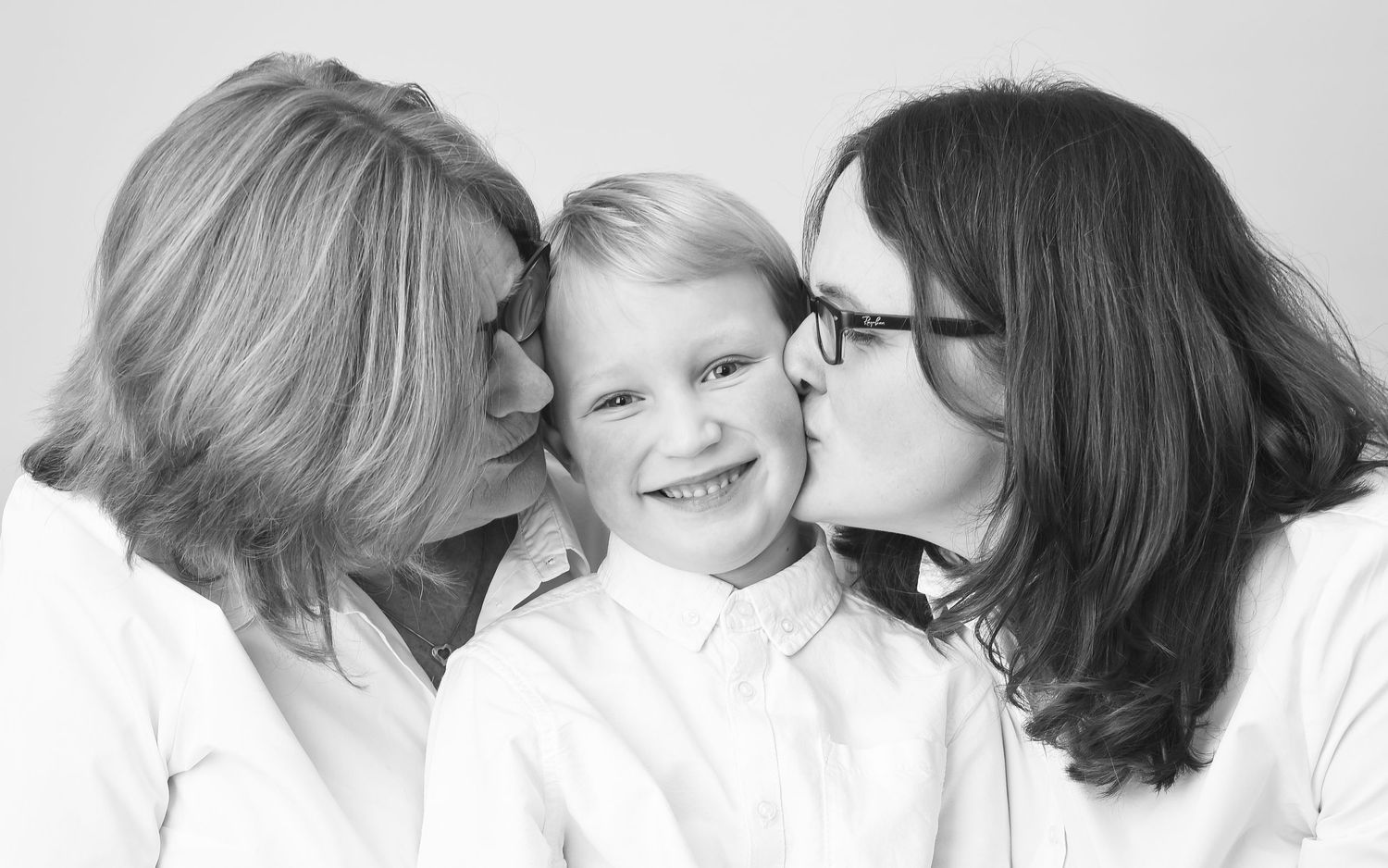 A mother and daughter kiss grandson on the check against a white background during a family photo shoot by Abigail's Studio High Wycombe.