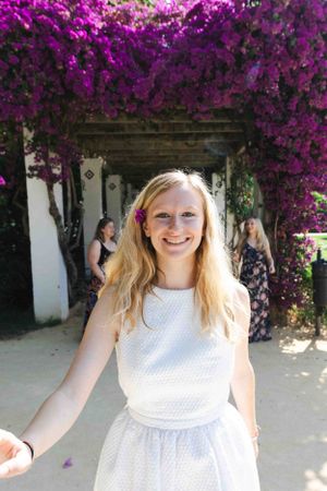 Beautiful flowering bougainvillea creates vibrant purple archway over white dress in sunny garden setting.