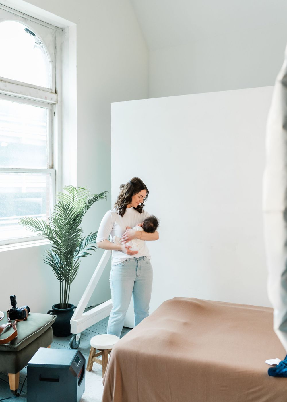 A minimalist nursery space features a potted palm plant by a bright window and neutral furnishings in soft tones.