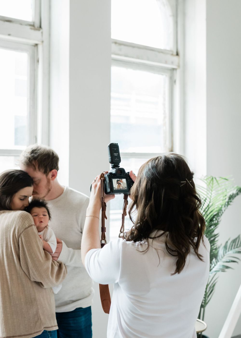 Behind the scenes view of photographer shooting a family portrait session in bright studio space with windows.