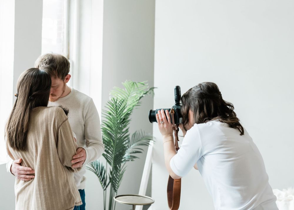 Behind the scenes shot of a professional photographer working in a bright studio with a palm plant and natural lighting.