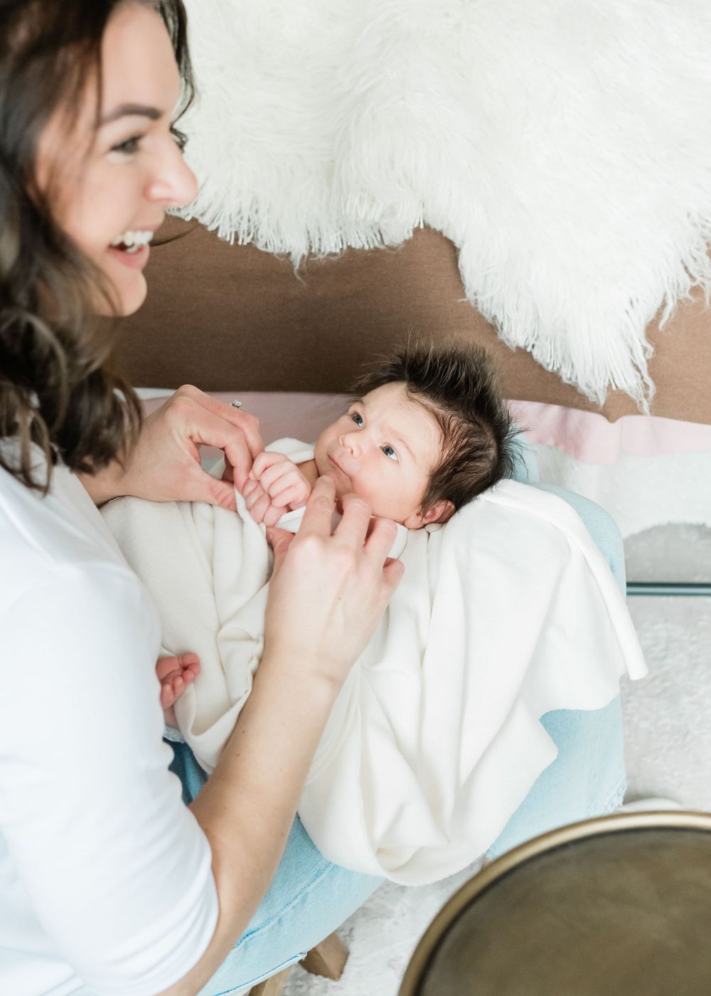 A tender moment between a woman in white and a newborn baby lying on soft white bedding.