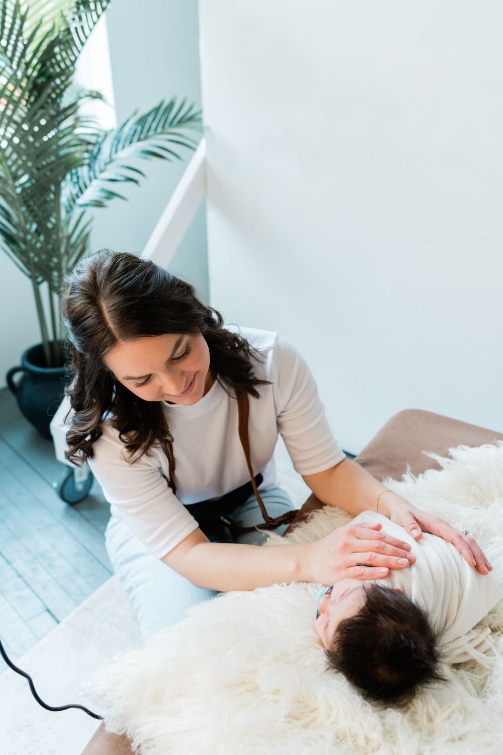 Professional massage therapist providing relaxing therapeutic treatment on soft white blankets next to indoor palm plant.