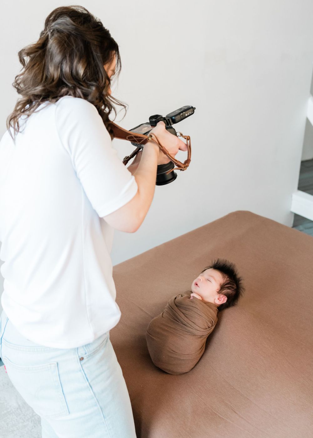 Photographer captures newborn baby swaddled in brown fabric on brown surface during professional photo session.