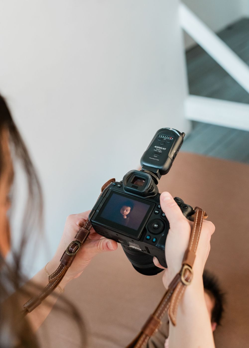 A photographer reviews photos on a DSLR camera's LCD screen while holding it with both hands indoors.