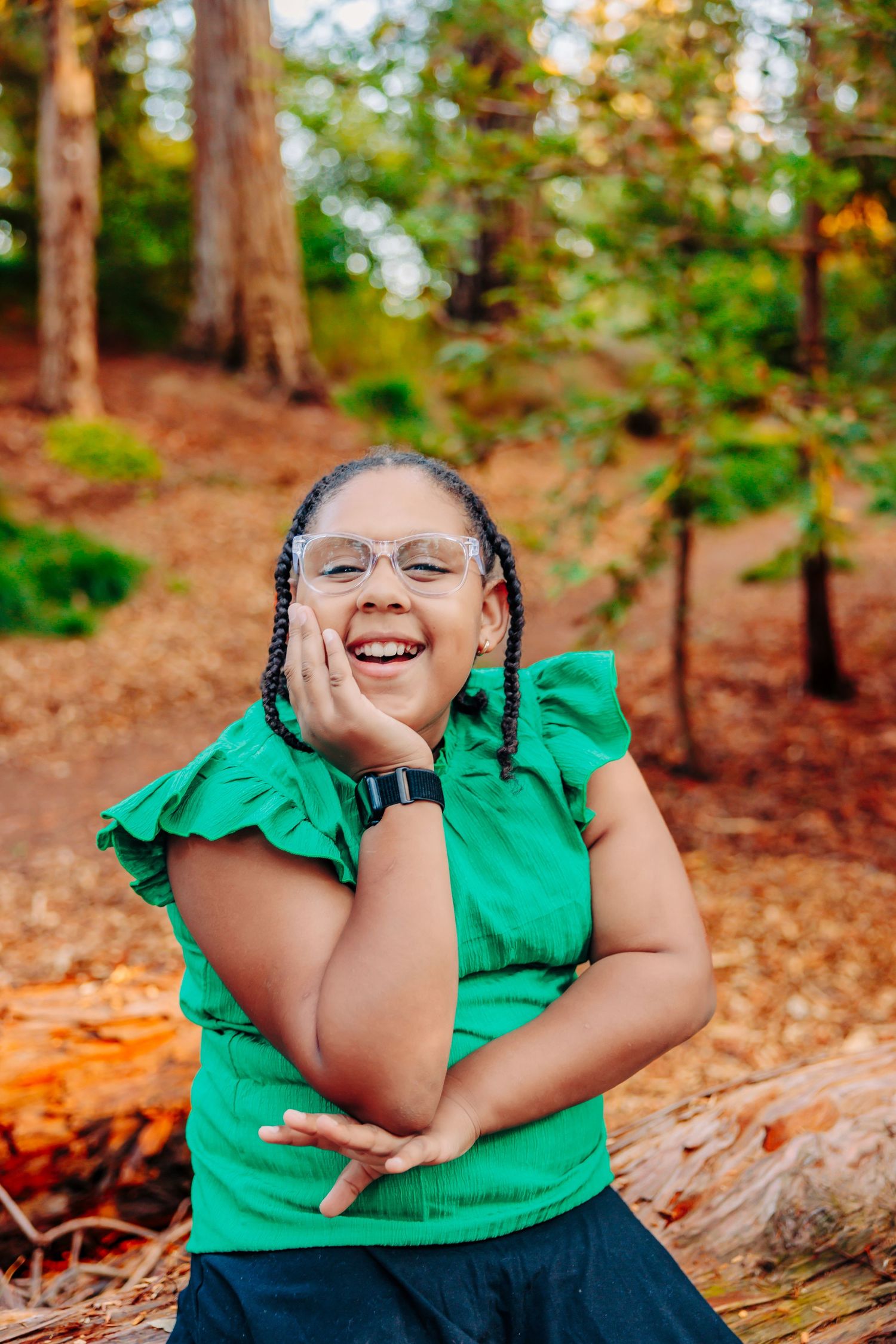 A person in a green shirt poses playfully on a fallen log in a wooded area with autumn foliage.