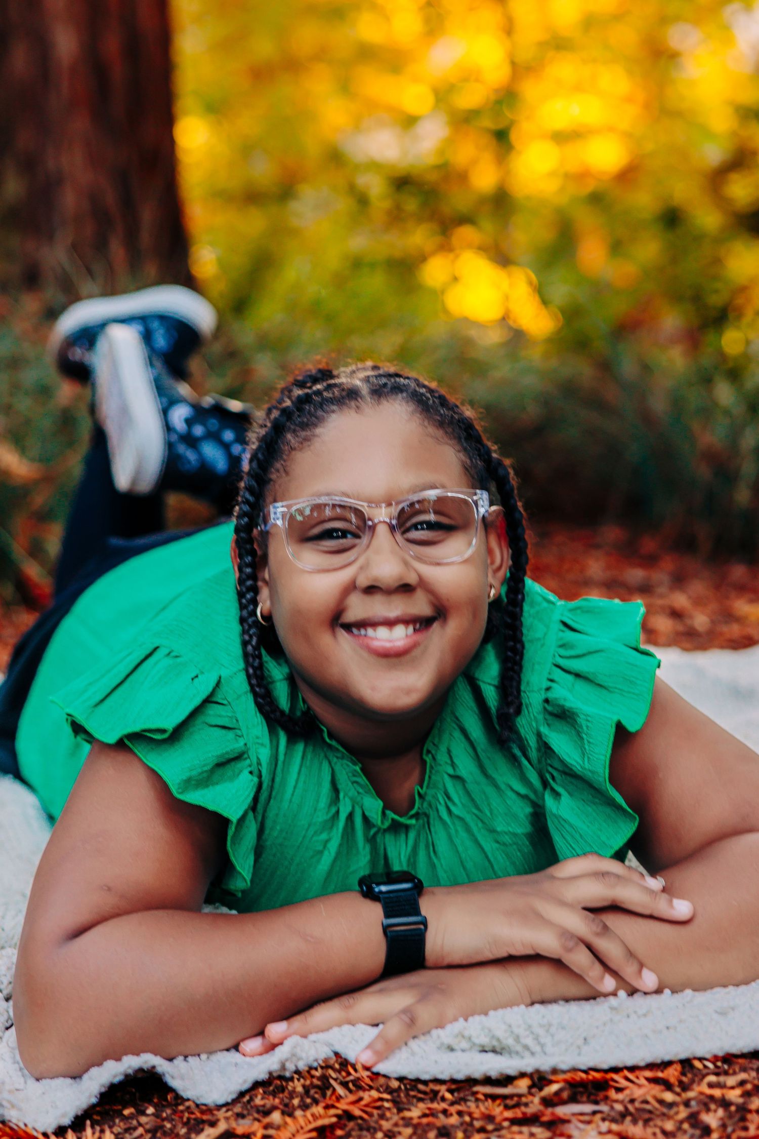 Someone in a bright green top lies on a white blanket surrounded by golden autumn foliage.