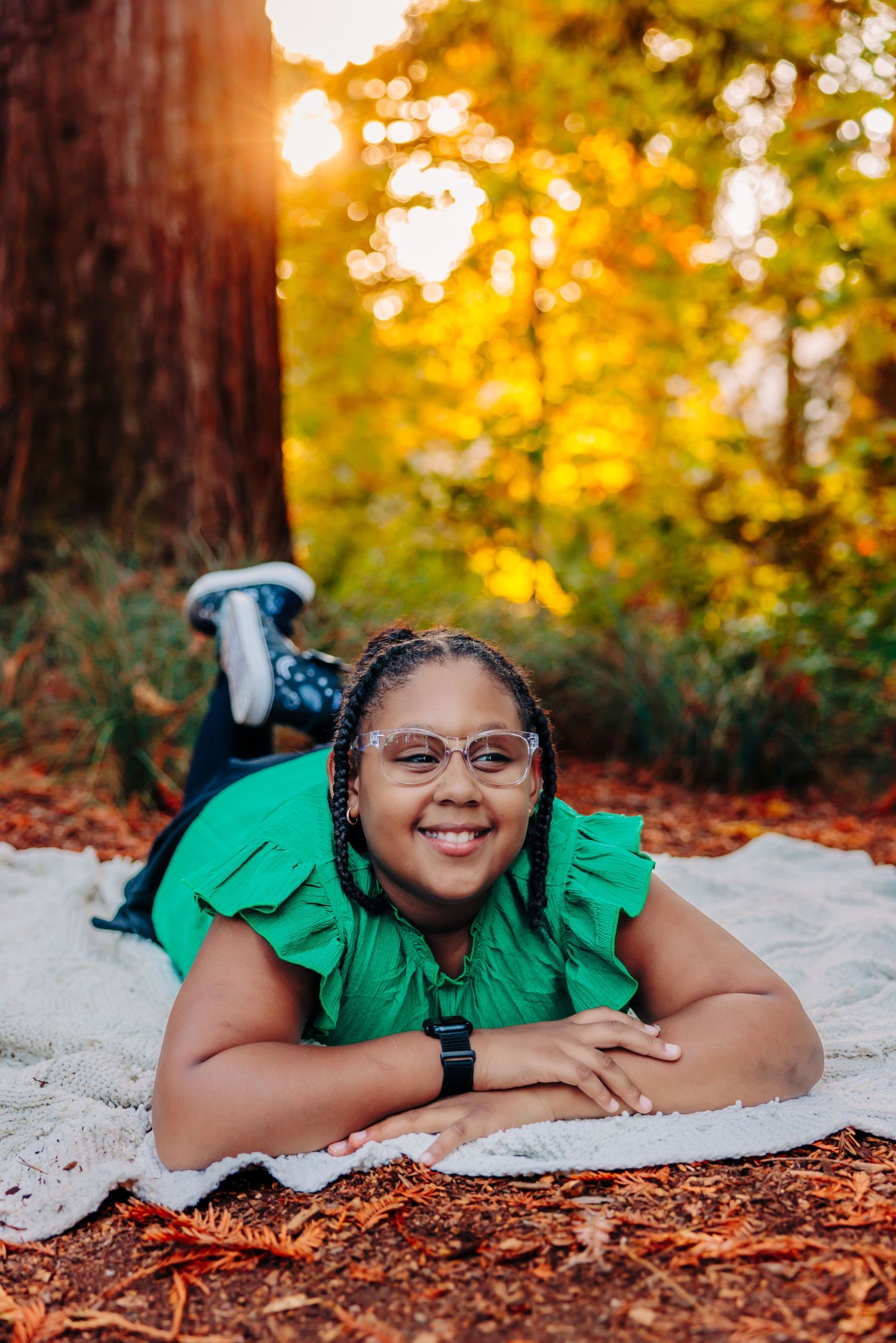 Portrait on a blanket in the woods during golden hour wearing a green top with ruffled sleeves.