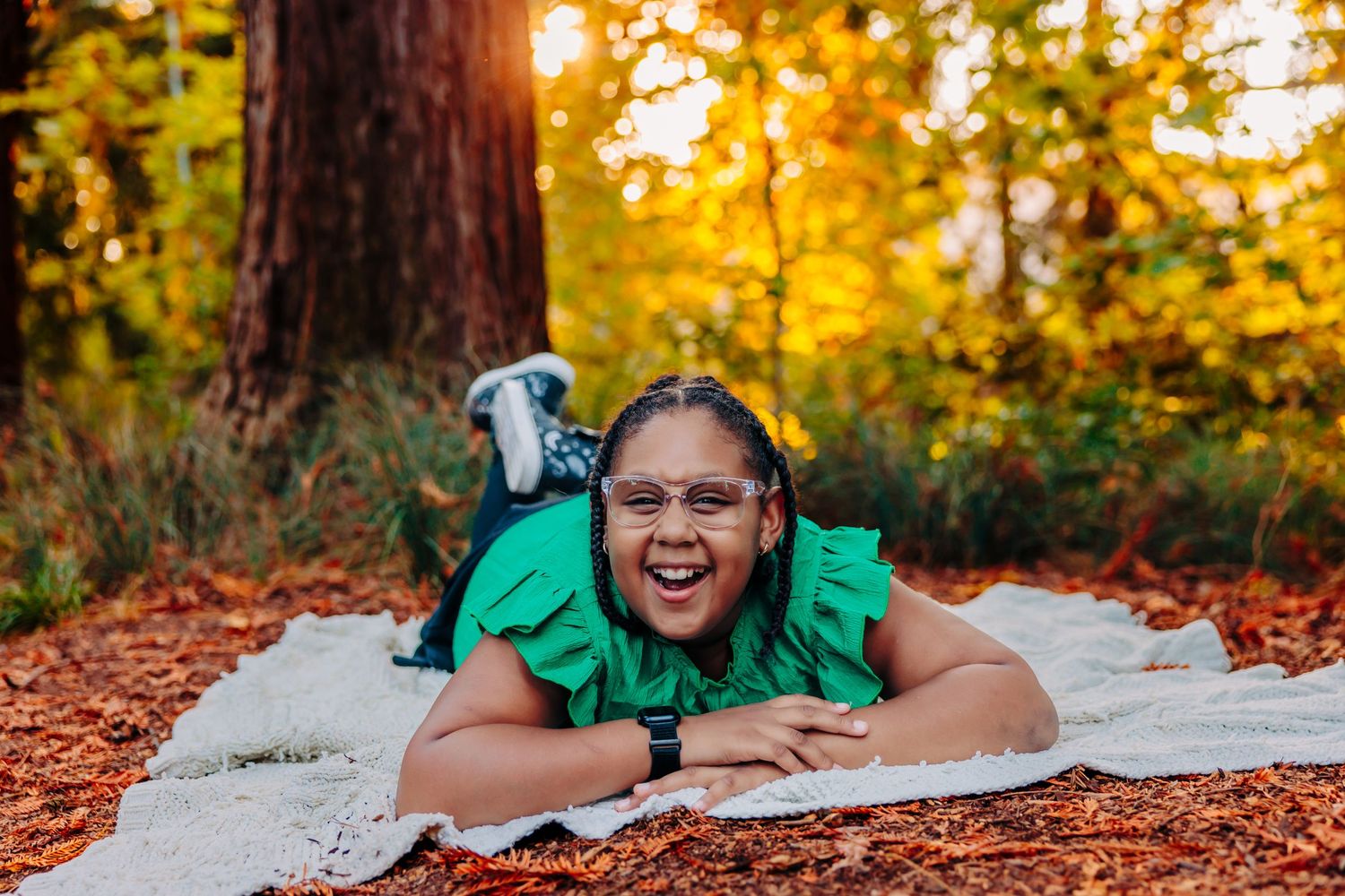 A person in a green dress lies on a white blanket surrounded by autumn leaves during golden hour sunset.