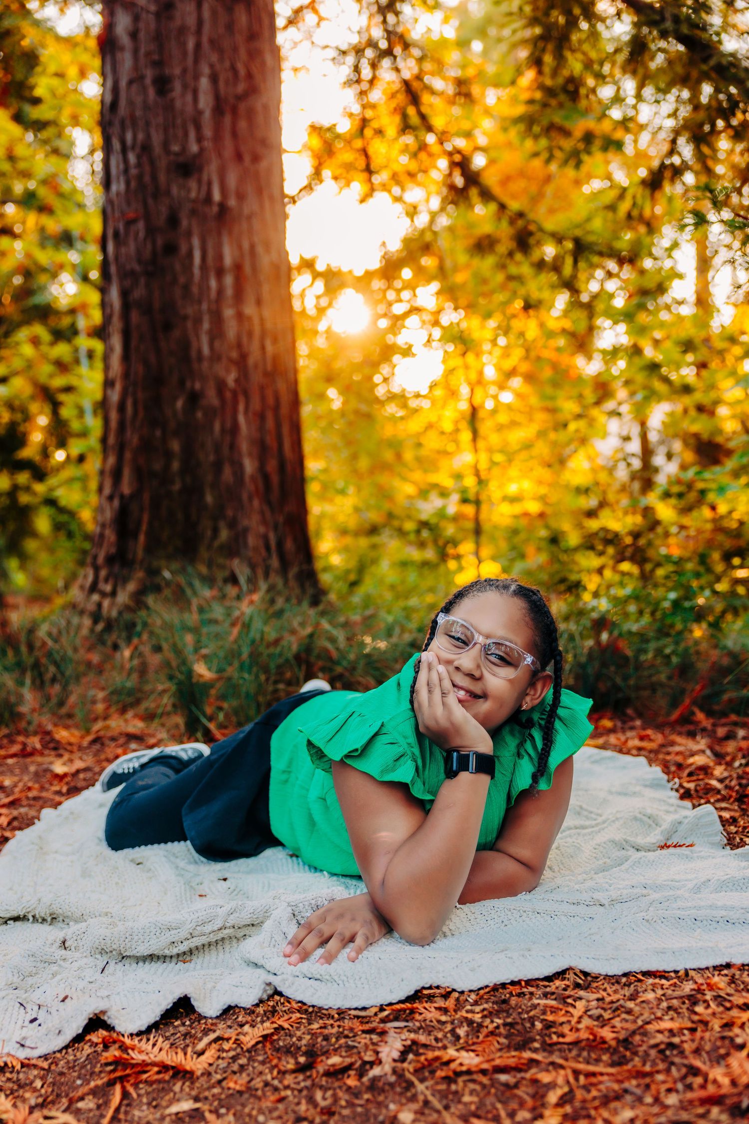 Relaxed pose on white blanket surrounded by fall foliage and redwood trees at sunset.