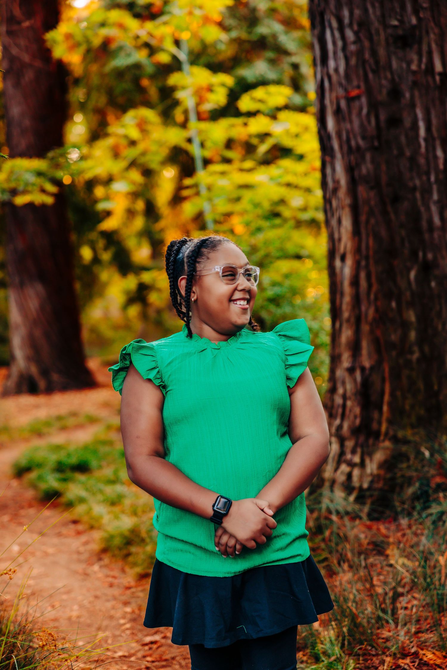 Person wearing green ruffled blouse smiles joyfully amid golden autumn trees and forest path.