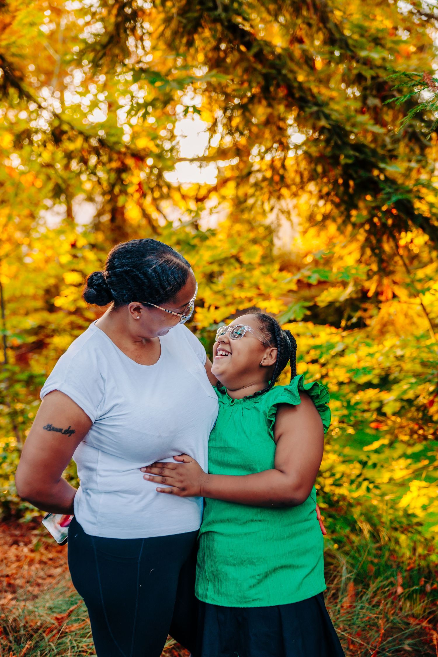 A joyful embrace between two people wearing green and white tops against a warm autumn forest backdrop.