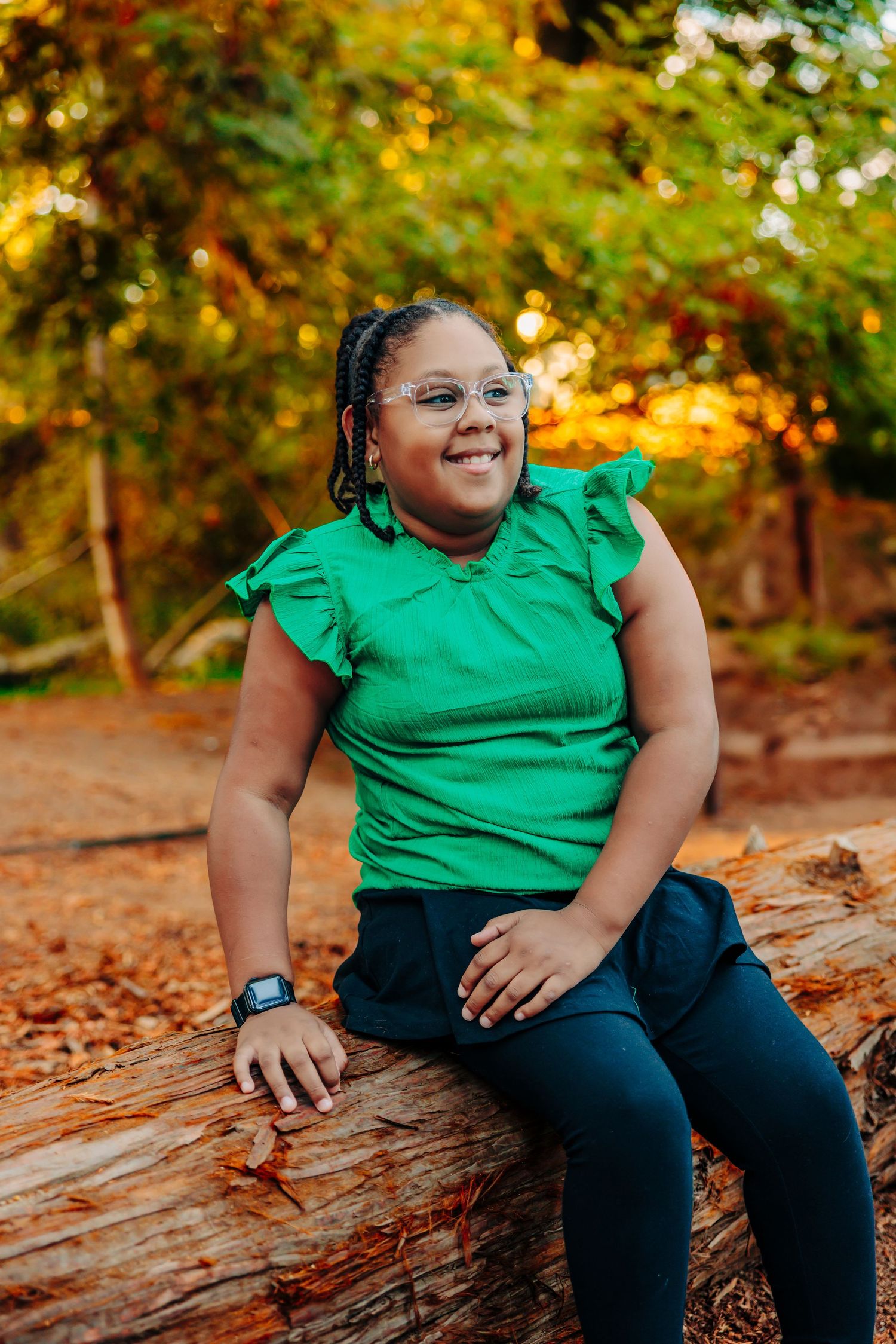 Person in bright green top sits on fallen log surrounded by autumn foliage in outdoor setting.