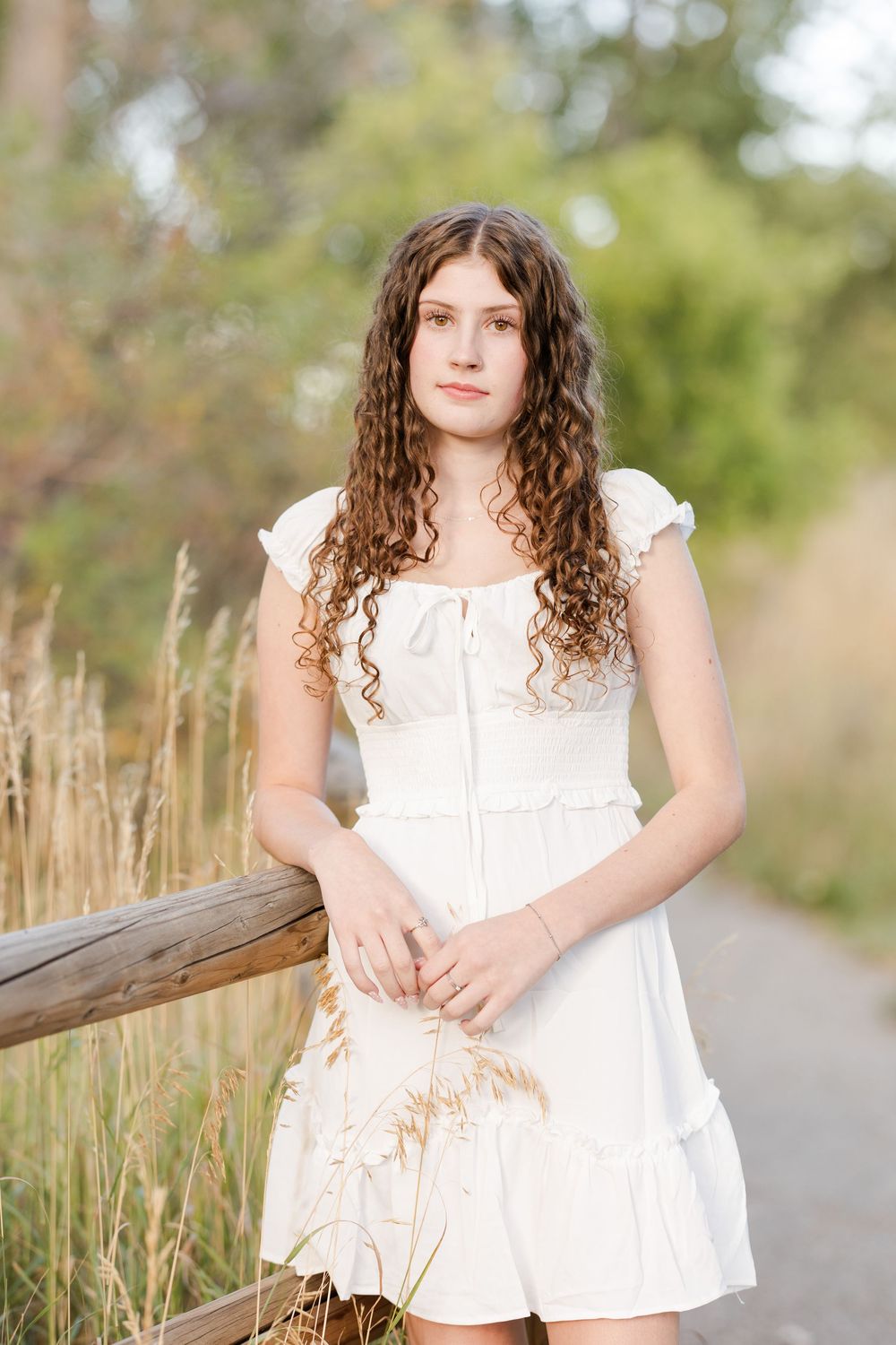 Natural light portrait featuring white dress and curly hair along rustic wooden railing.