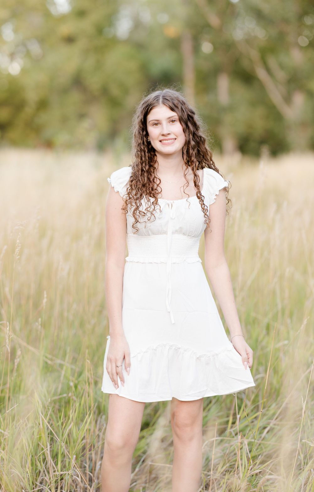 A white summer dress with short sleeves stands out against tall grass in a sunlit outdoor setting.