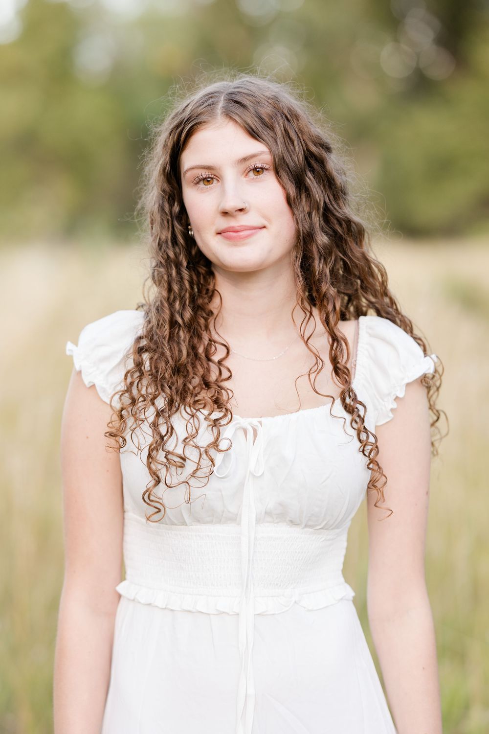 Person in white dress with curly hair poses in outdoor portrait series against blurred natural background.