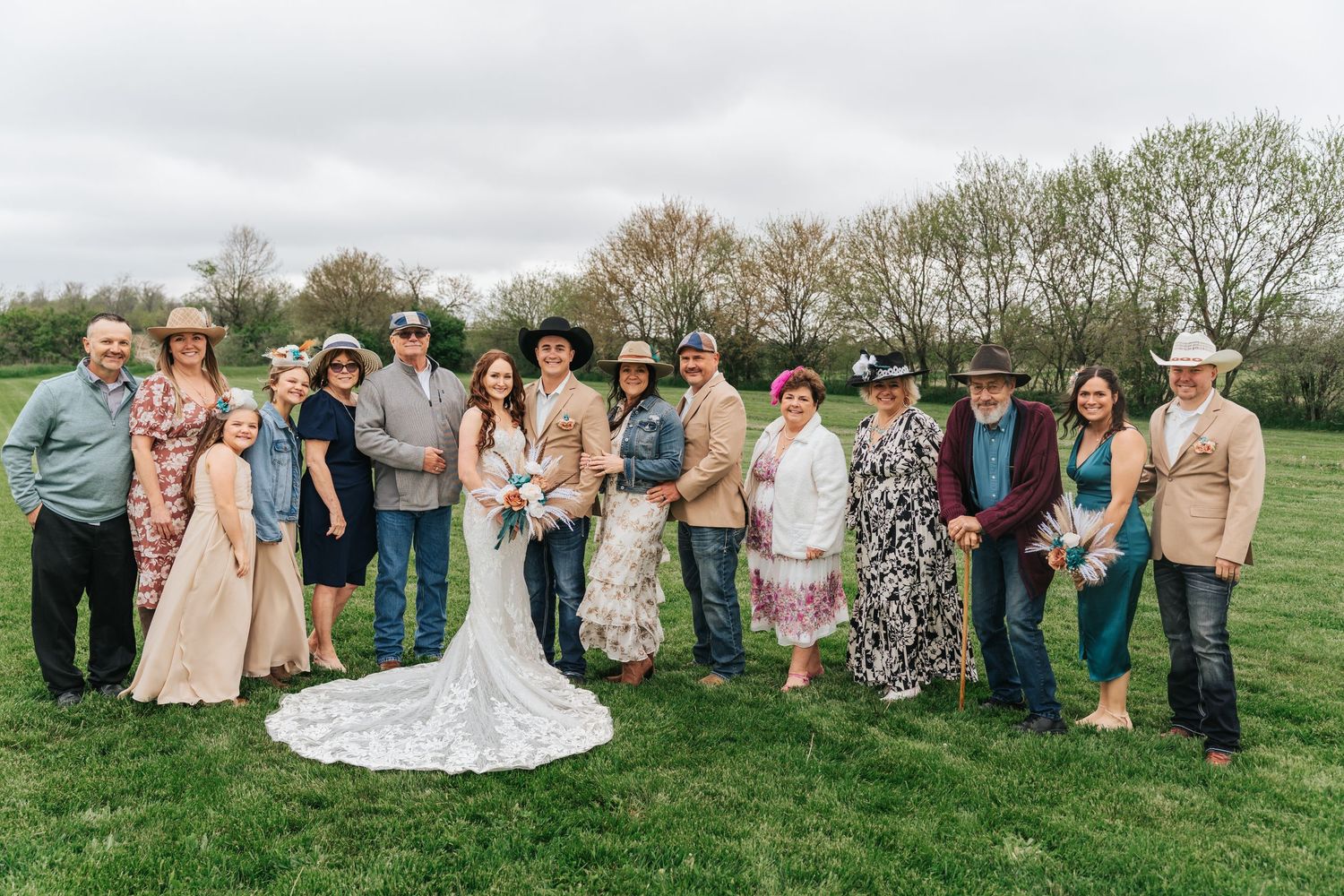 Wedding party gathers on a lush green hillside for outdoor group photos during spring celebration.
