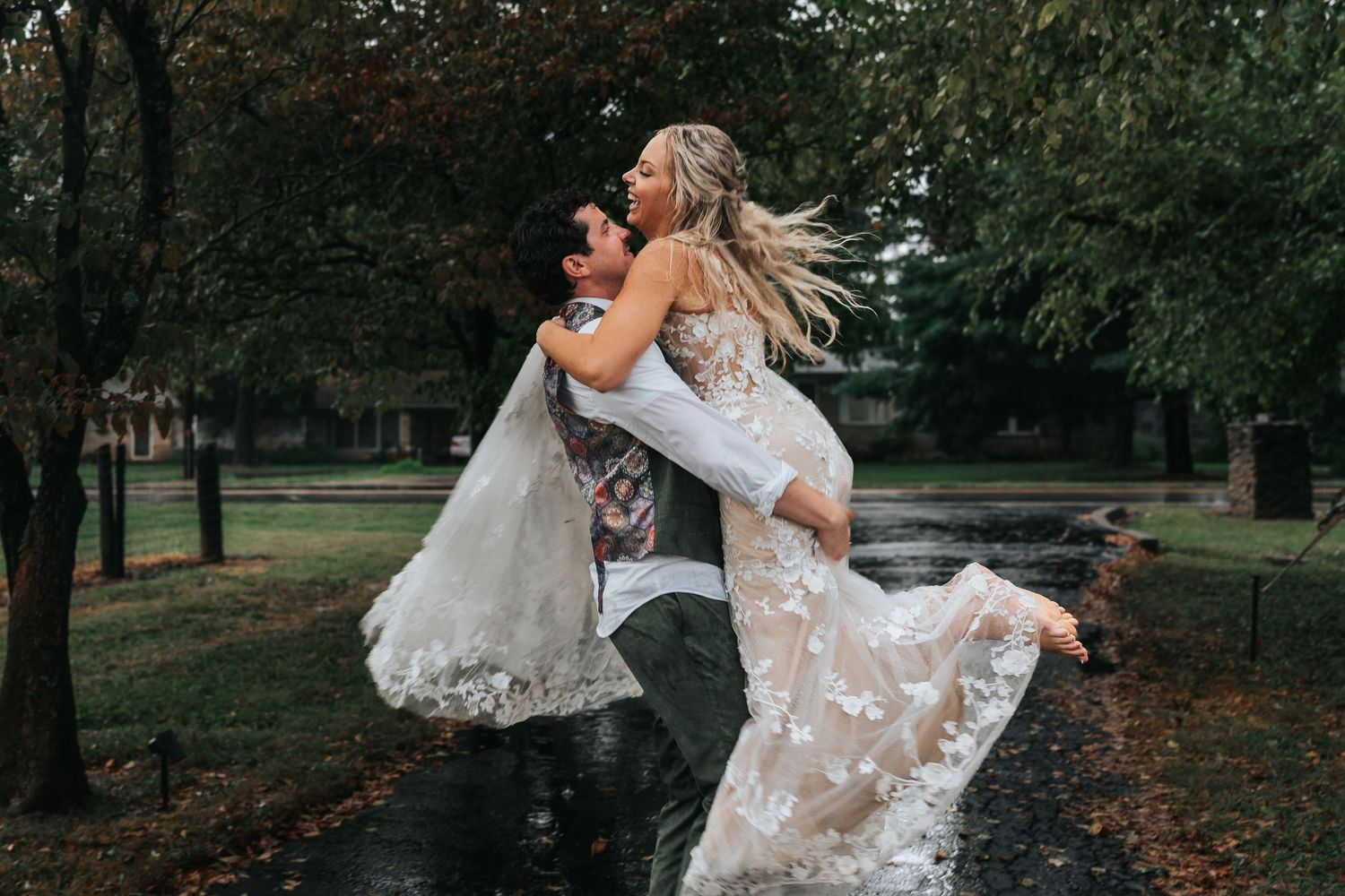 A couple in wedding attire dances together in a romantic embrace at an outdoor park during autumn.