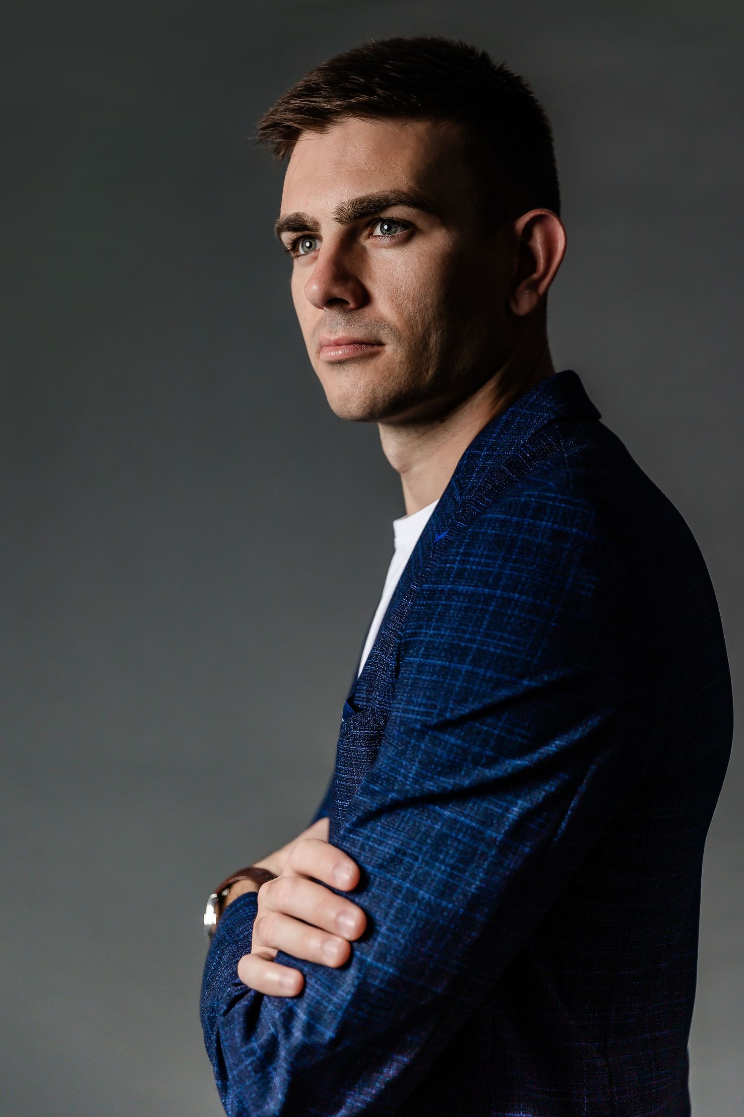 Portrait of someone in a light blue button-down shirt leaning against a wall in an urban setting.