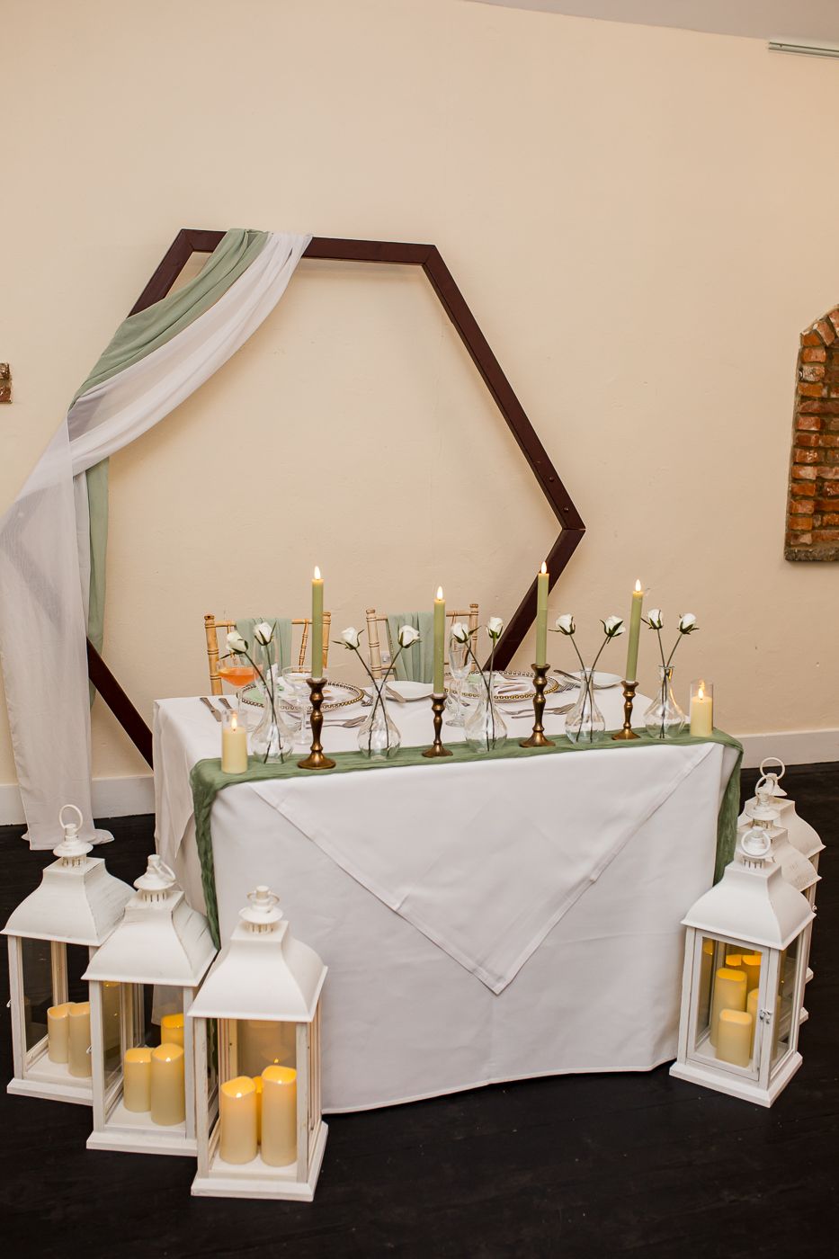 White lanterns and candles line a decorated head table with sage green accents.