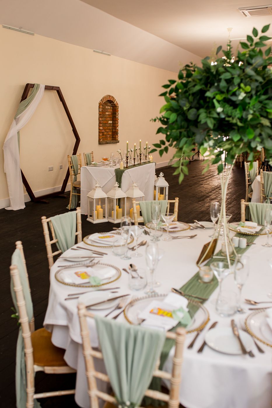 Wedding reception tables set with white linens, sage green accents, and elegant place settings.