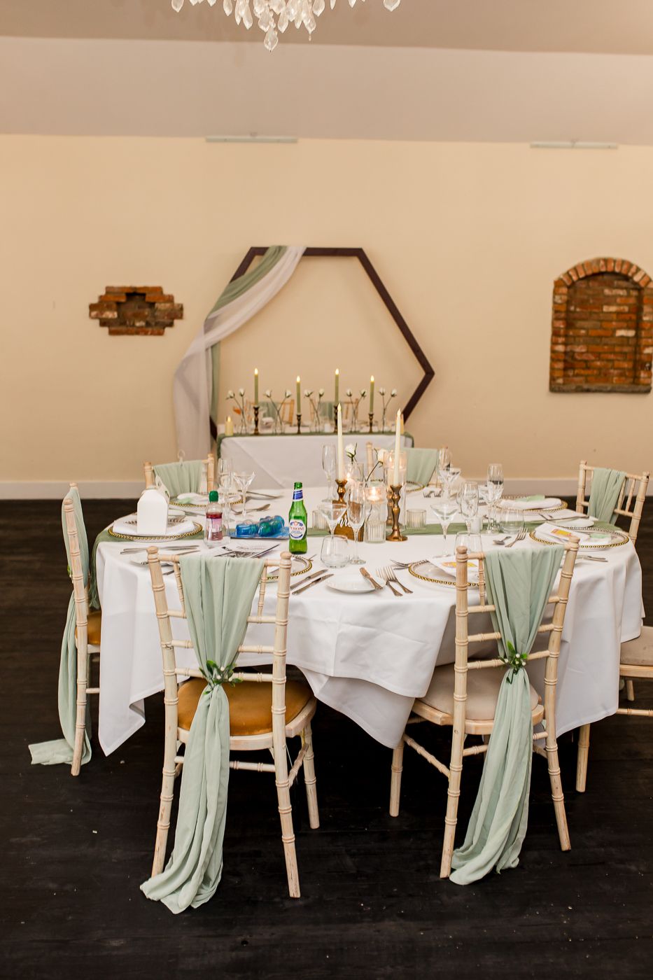 Elegant dining tables with sage green chair sashes and white tablecloths at a wedding reception.