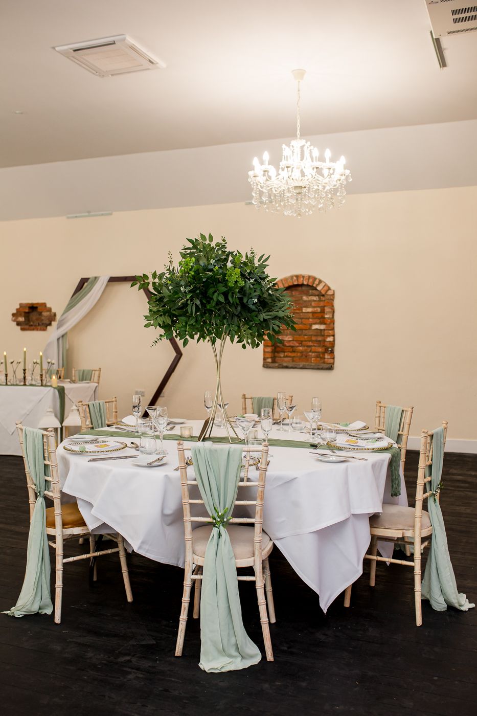 Wedding reception venue with crystal chandelier and tables decorated in white and sage green.