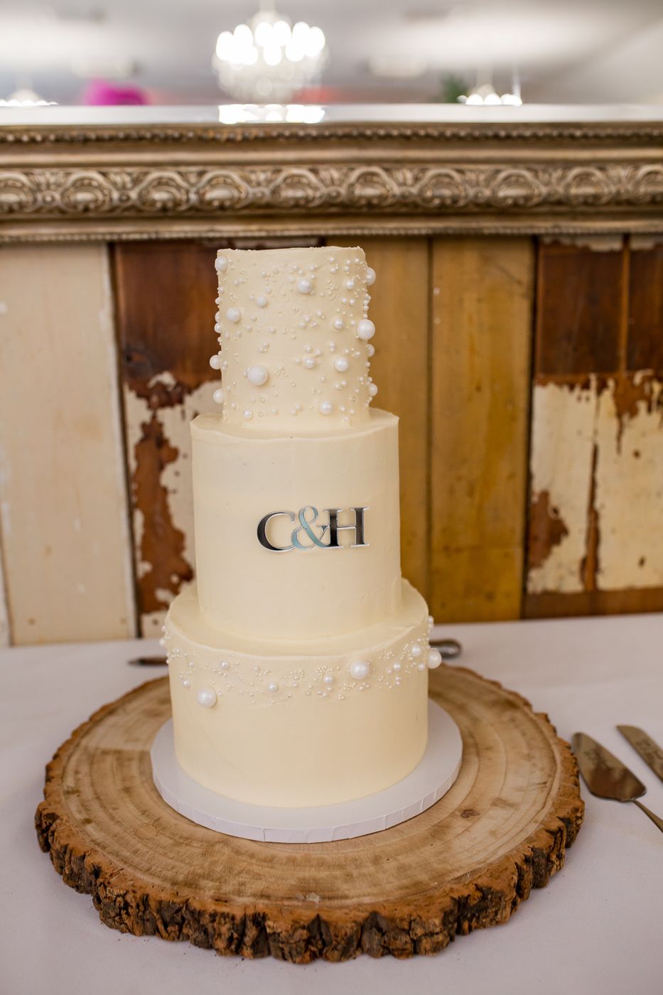 Simple white wedding cake displayed on a rustic wood slice with initials on top.
