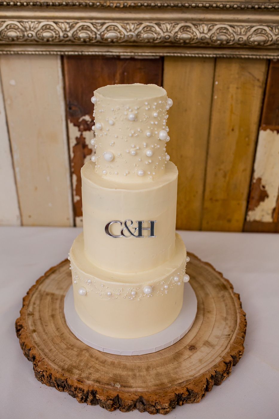 Simple white wedding cake with monogram initials displayed on rustic wood slice cake stand.