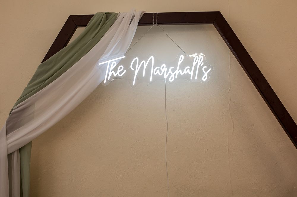 Illuminated neon wedding sign mounted on wall with white fabric draping.