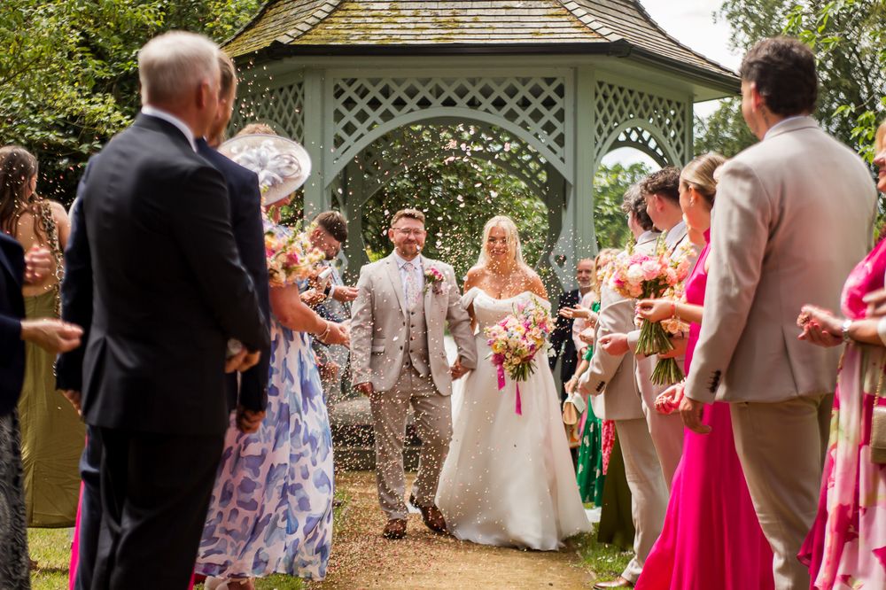 Outdoor summer wedding celebration with guests in bright dresses near garden gazebo.