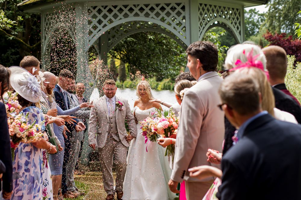 Wedding celebration with guests in colorful attire gathered around a white latticed gazebo.