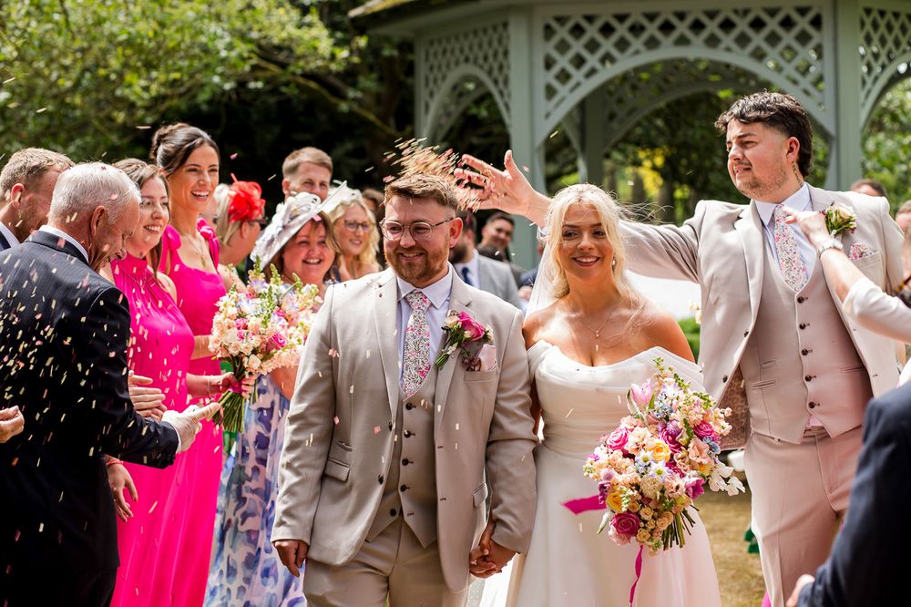 Joyful wedding celebration with guests in bright colors around a garden gazebo.