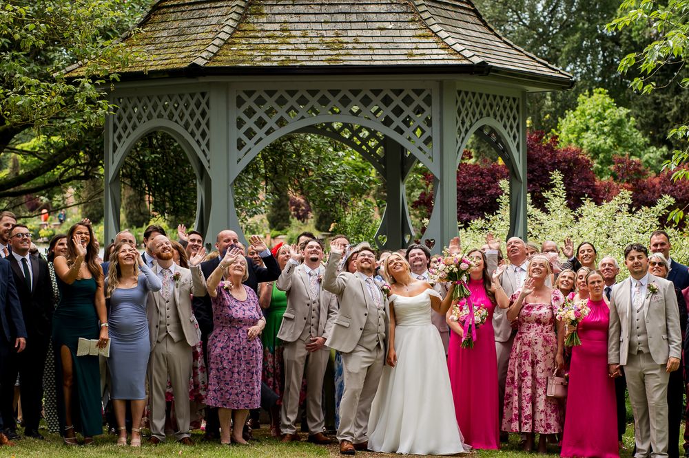 Large wedding party poses for a group photo in front of a garden gazebo.