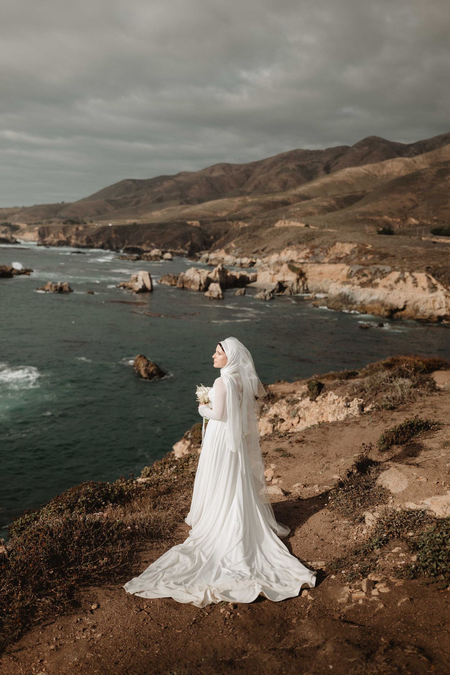 an indian bride standing on the cliffs holding her bouquet overlooking the ocean