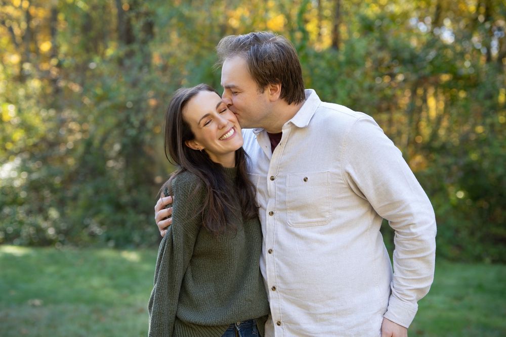 Husband & Wife kiss at fall foliage family portraits in Greater Boston. Photography by Leah Ramuglia at the Wayside Inn Grist Mill, Sudbury.
