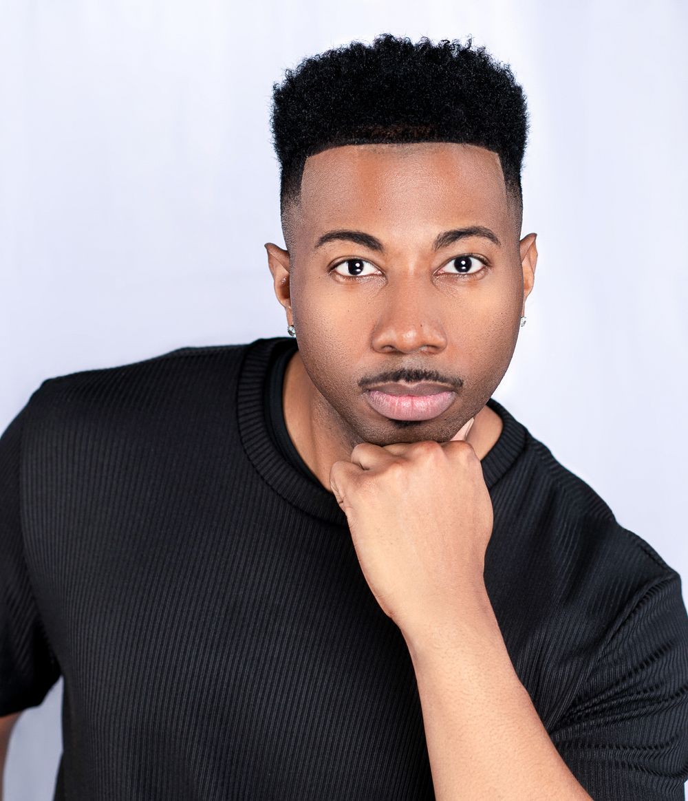 Professional headshot portrait of someone wearing a black shirt against a white background with a contemplative expression.