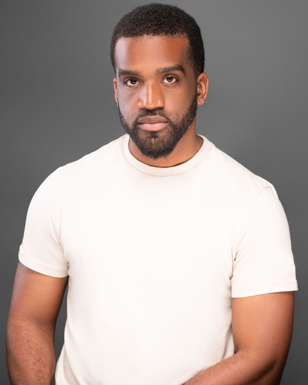 A person wearing a white t-shirt poses against a gray background in a professional headshot series.