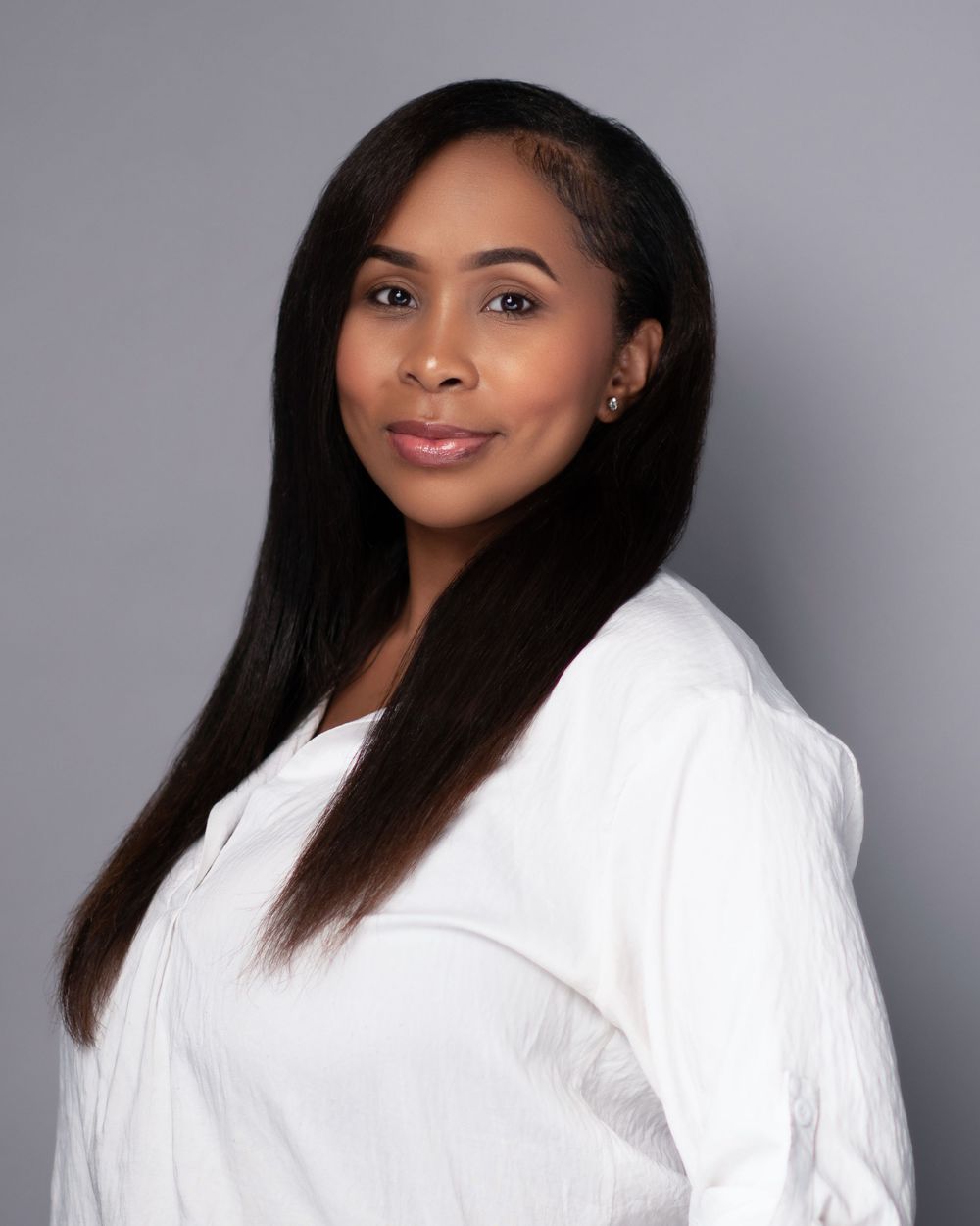 Professional headshot portrait of someone wearing a white top against a gray background with long straight dark hair.