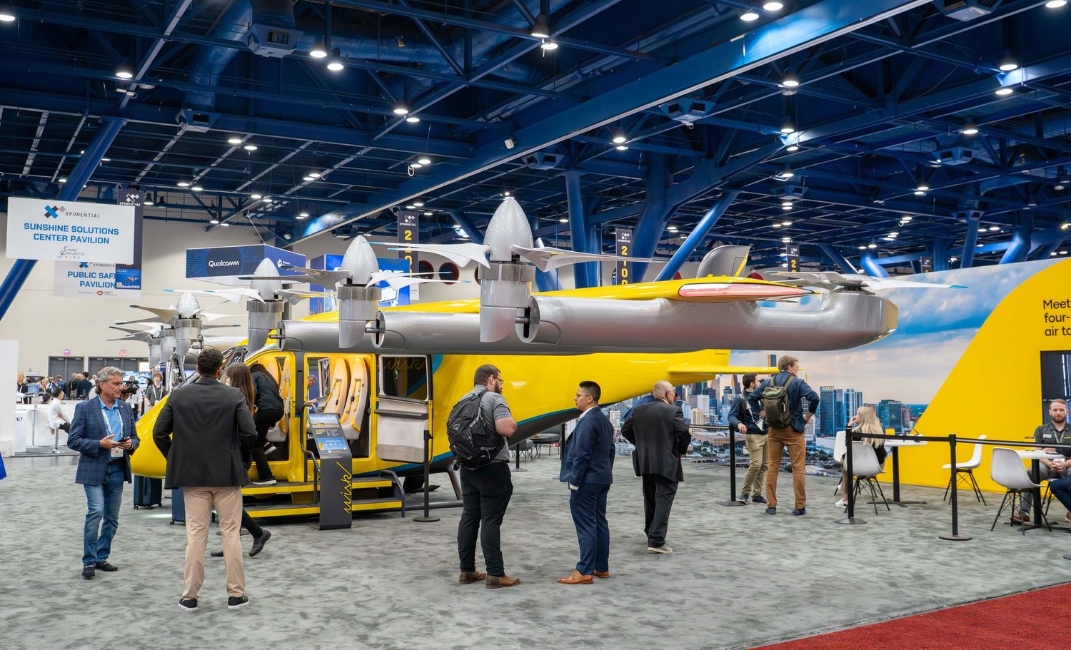 A row of yellow and blue aircraft displayed at an indoor aviation exhibition with attendees viewing the planes.