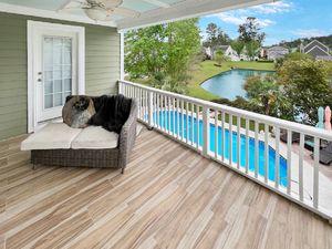 Covered deck with white railings overlooking a swimming pool and landscaped yard.