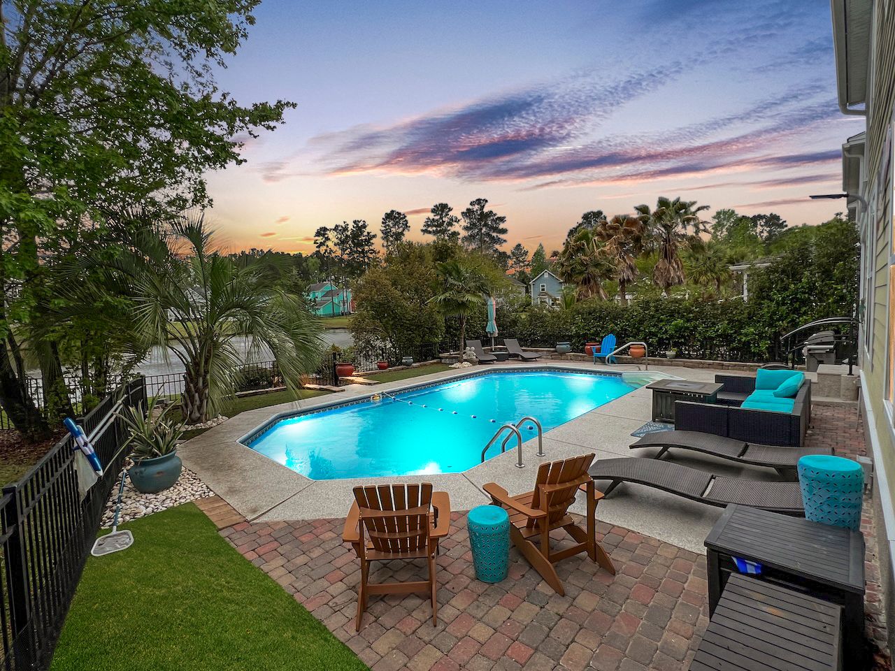 Panoramic view of a backyard oasis with pool, deck, and scenic sunset backdrop.
