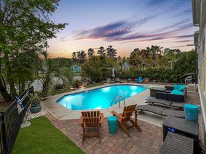 Panoramic view of a backyard oasis with pool, deck, and scenic sunset backdrop.