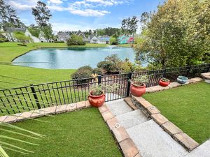 Backyard patio area overlooking a serene pond with decorative railing and outdoor seating.