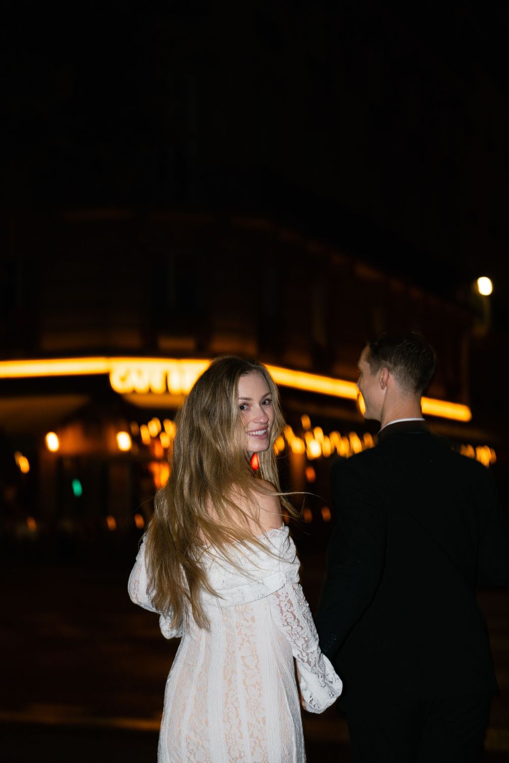A couple dances together at night under warm glowing lights creating a romantic atmosphere. Paris film photographer.