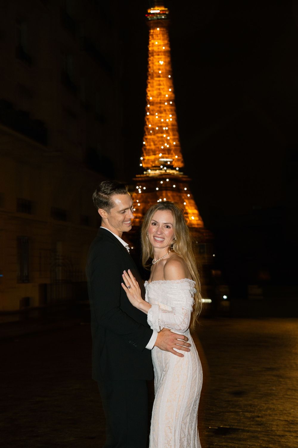 Romantic couple dancing at night with illuminated Eiffel Tower glowing in the background in Paris. Paris film photographer.