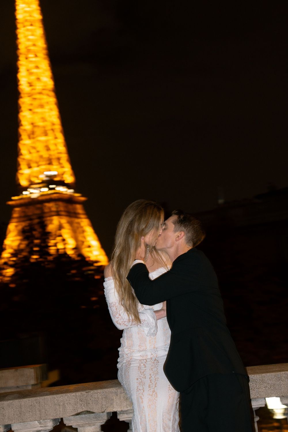 A romantic couple shares an intimate moment at night with the illuminated Eiffel Tower glowing in the background.
