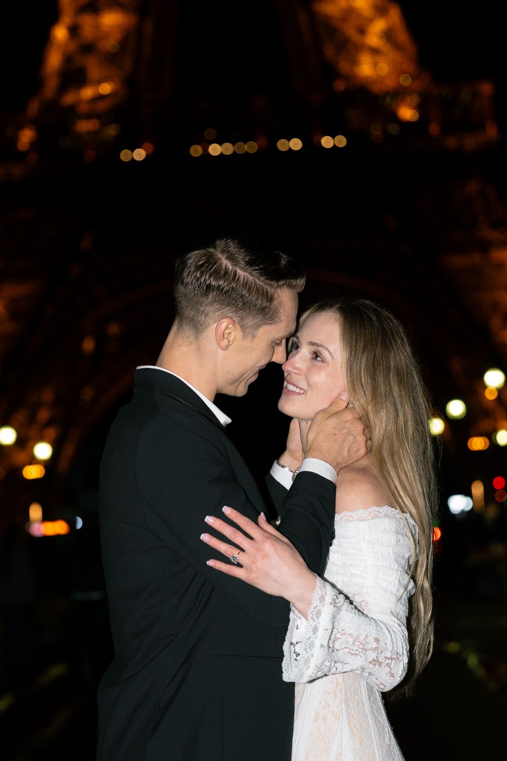 A romantic nighttime moment between a couple in formal attire sharing an intimate embrace under city lights.