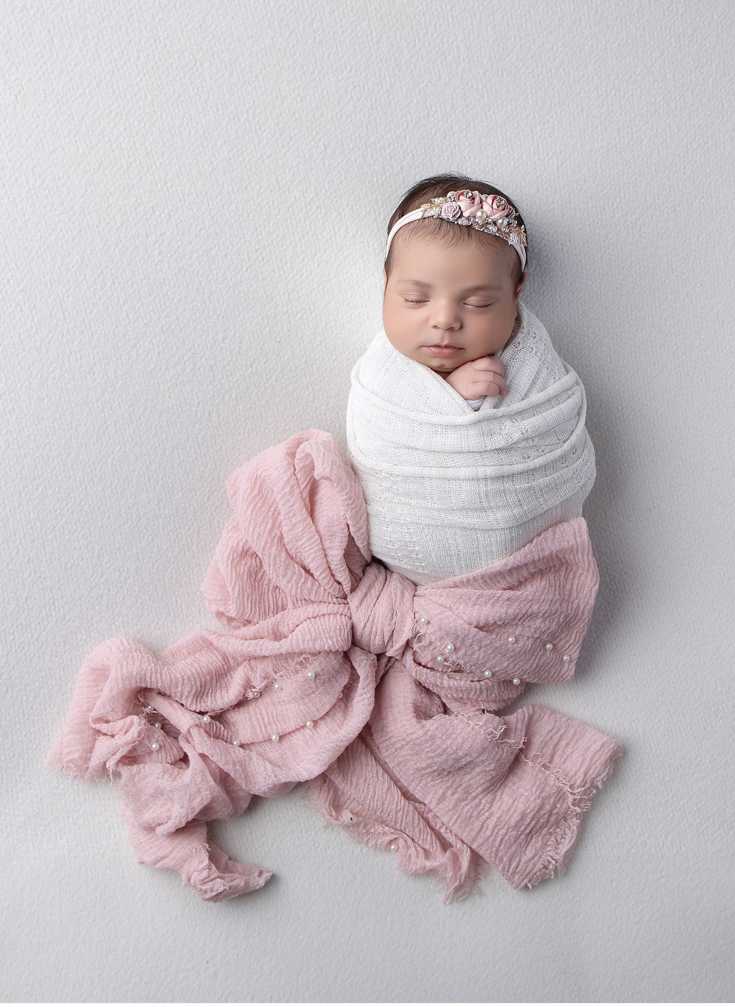 Wrapped newborn baby posed on soft pink fabric backdrop in Austin newborn photography studio